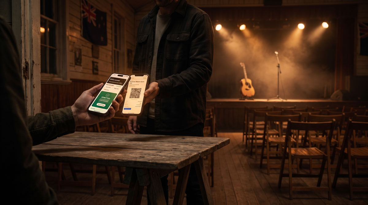 A phone scanning a QR ticket at the door of a dimly lit country hall, with an acoustic guitar on a warmly lit stage in the background.